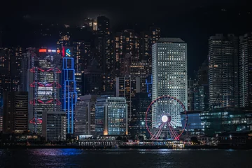 Dense Hong Kong buildings and a bright Ferris wheel along the harbour at night