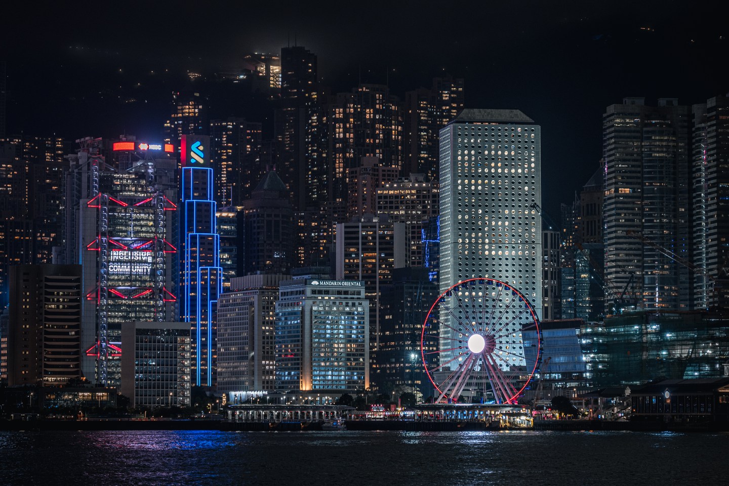 Dense Hong Kong buildings and a bright Ferris wheel along the harbour at night