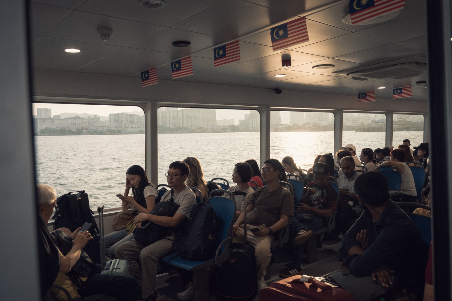 Passengers inside a ferry cabin, with daylight through the windows
