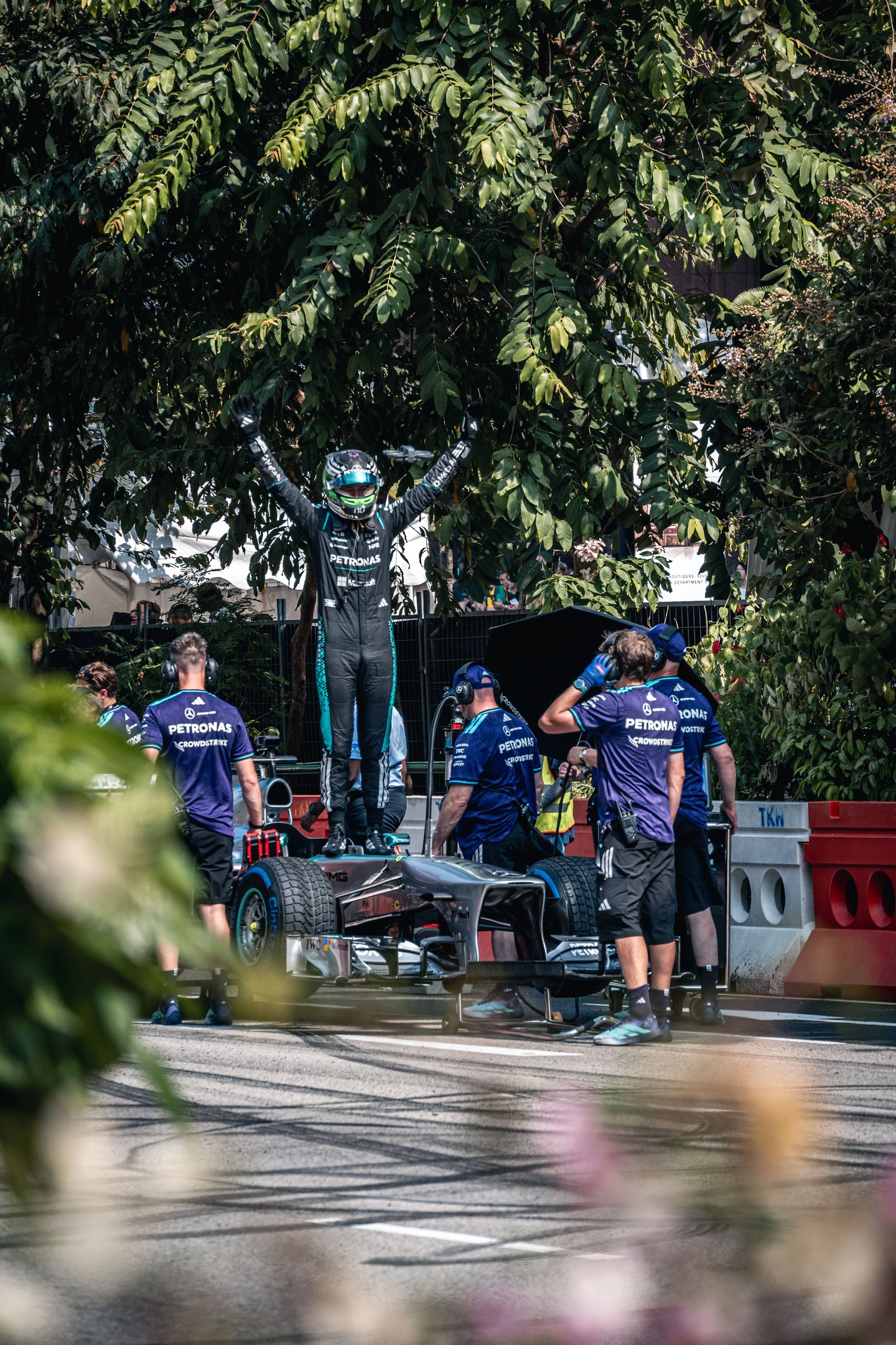 A helmeted driver raising both arms beside a Formula 1 car