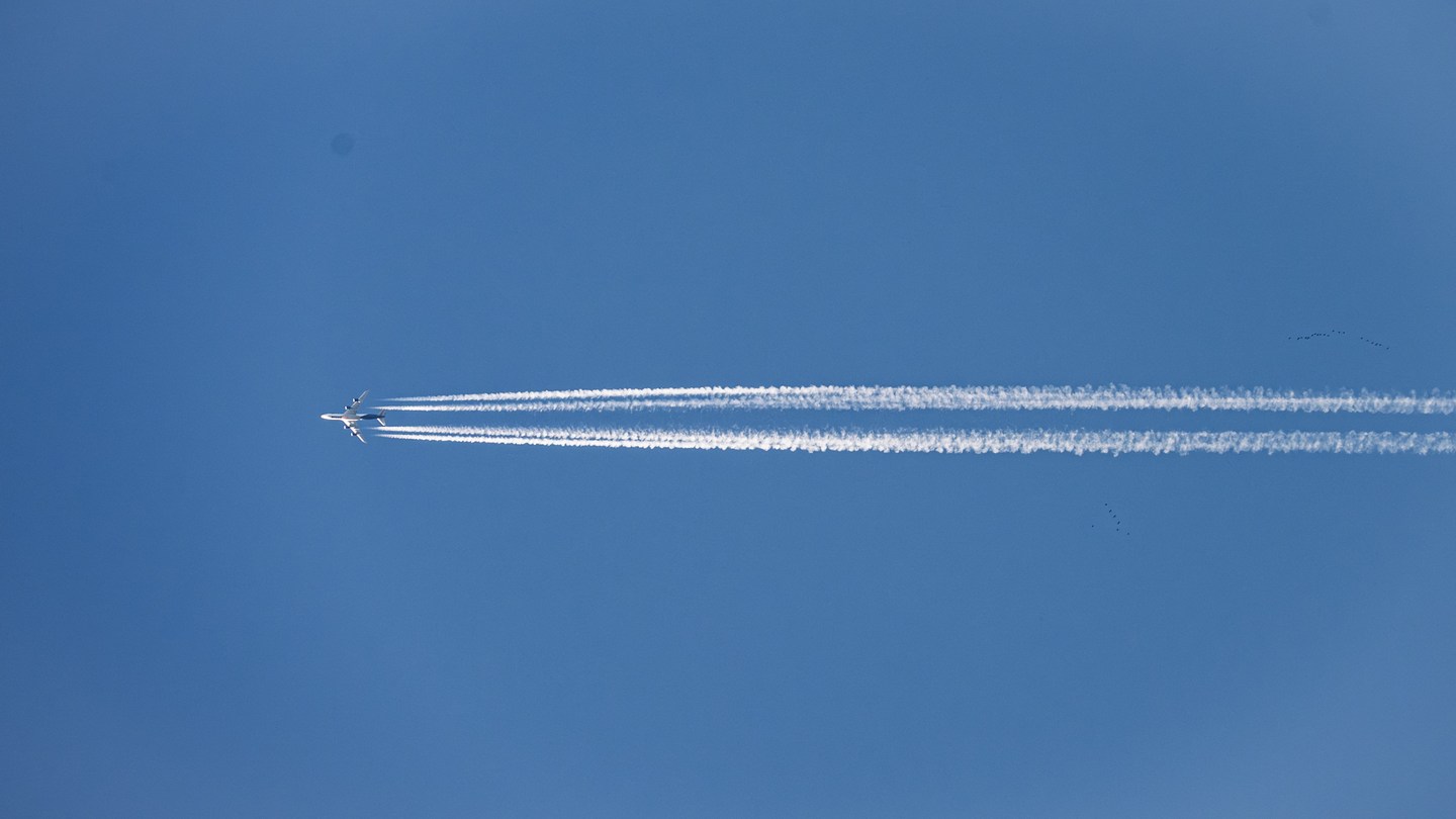 A distant aircraft trailing parallel white contrails across a blue sky