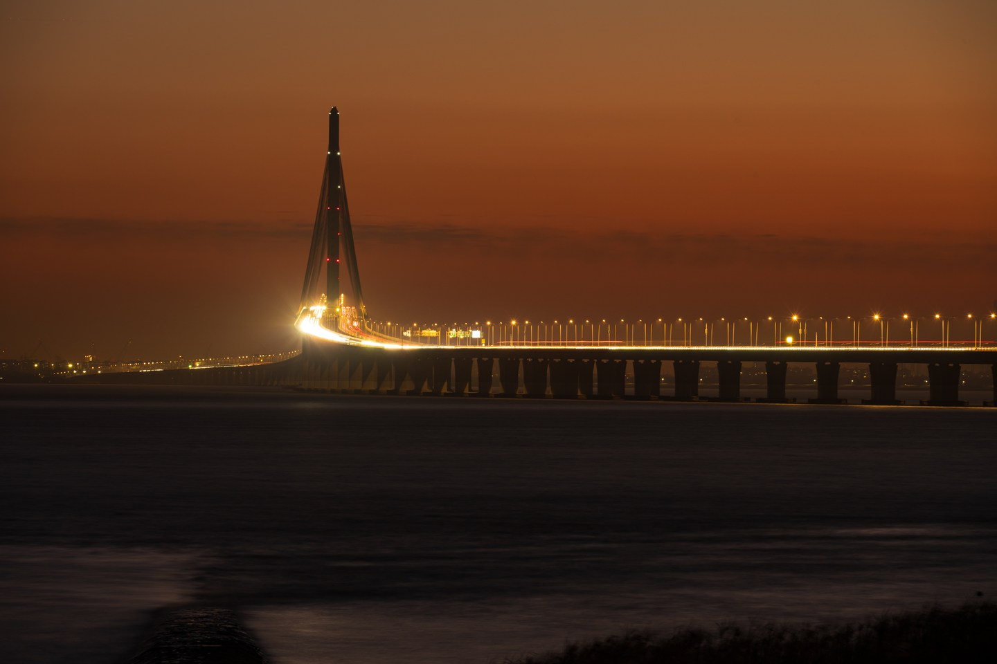 An illuminated bridge spanning the water at dusk