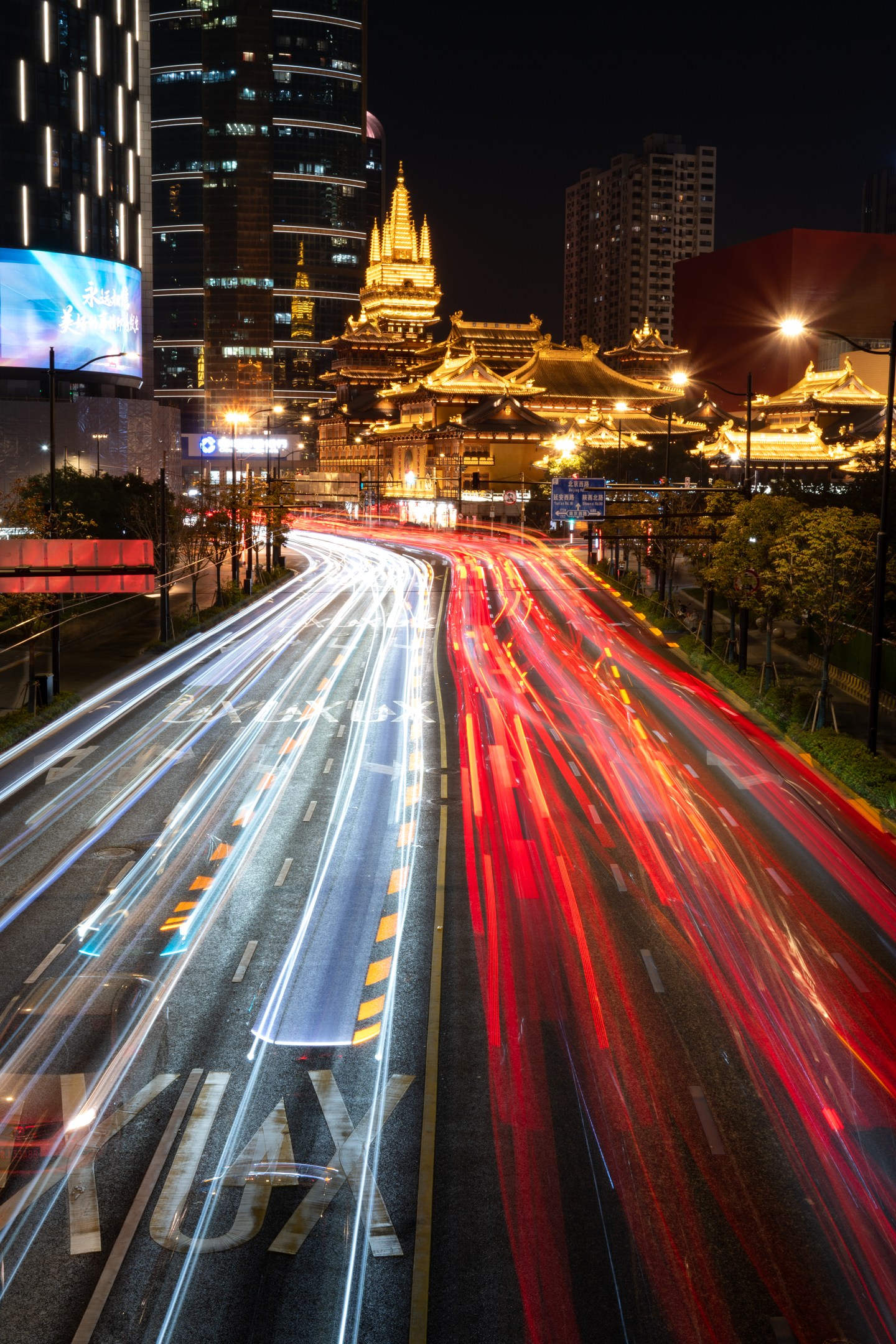 Traffic light trails leading past an illuminated temple in Shanghai