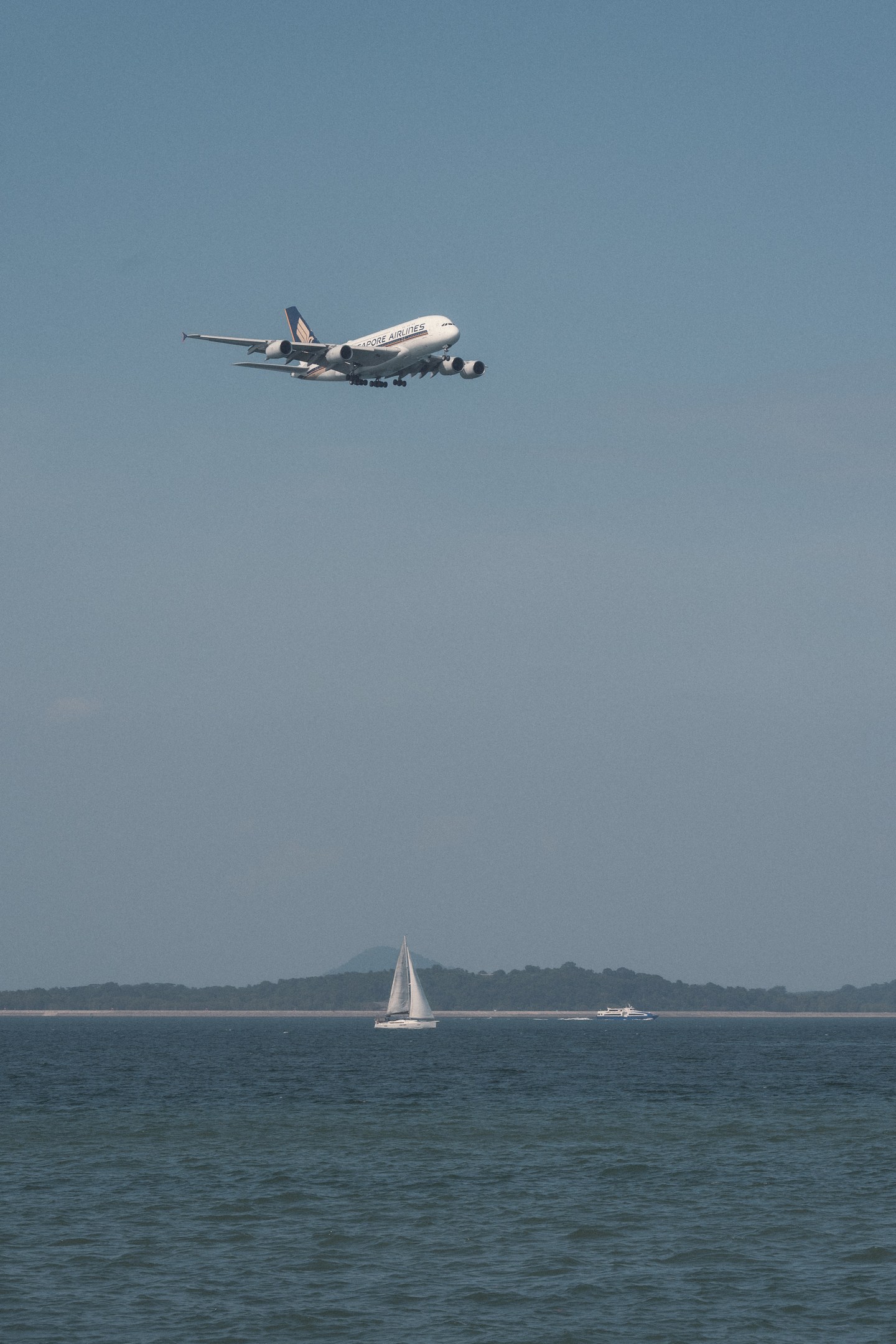An aircraft above the sea with a small sailboat below